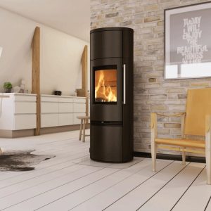 Runder schwarzer Kaminofen mit sichtbarem Feuer, daneben ein gelber Holzstuhl und ein Bild mit Text an einer Ziegelsteinwand.